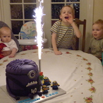 Firework candle lit on Purple Evil Minion cake with grandchildren watching